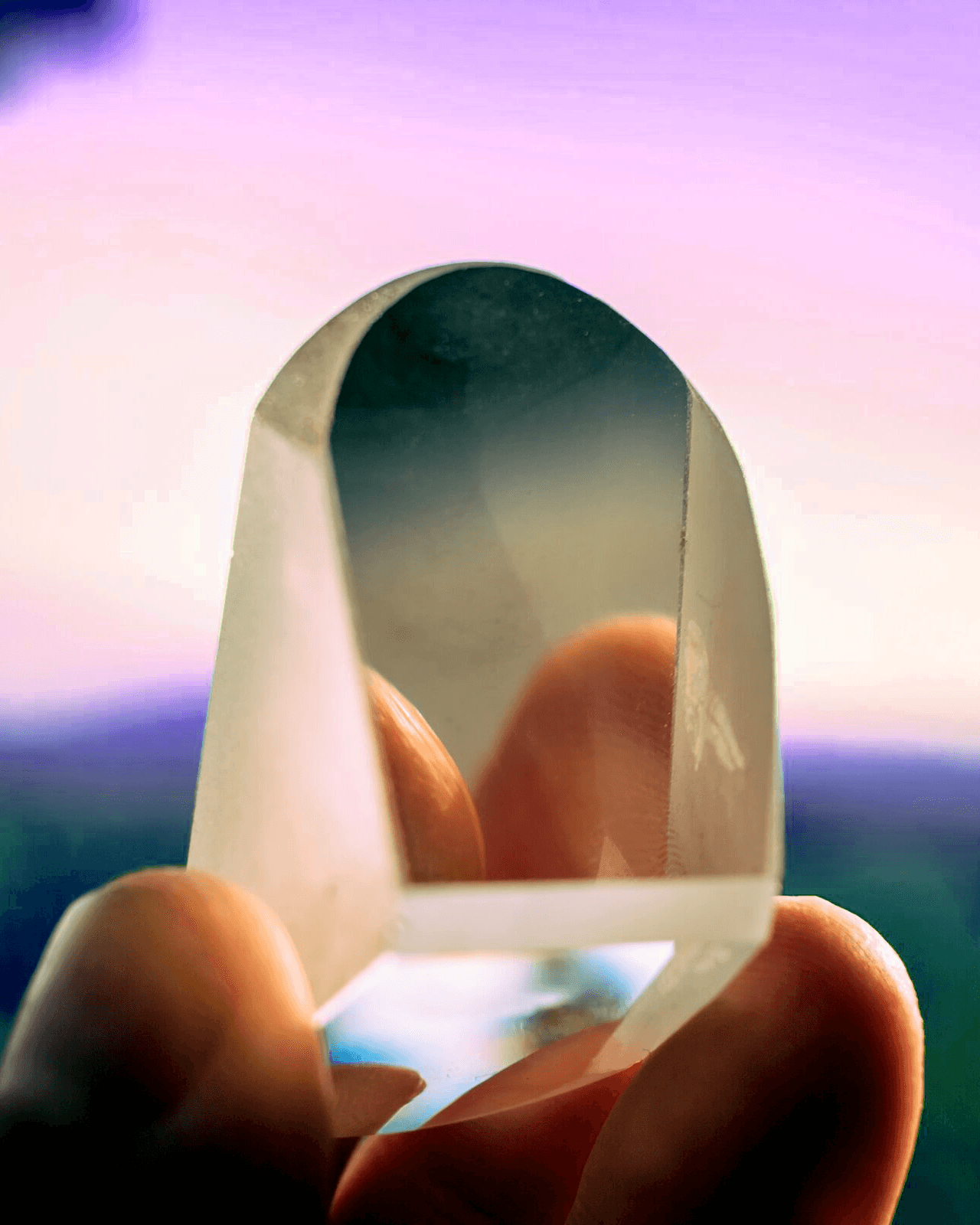 crystal held between fingers against a pink sky