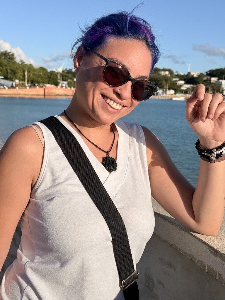 Joa at the waterfront in Puerto Rico, wearing sunglasses and a hexagon necklace.